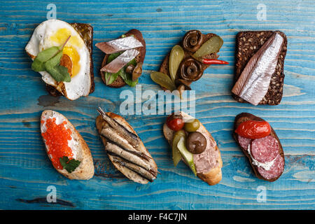 Verschiedene belegte Brötchen aus Vollkorn Baguette und Schwarzbrot mit verschiedenen Belägen über Alter blauen hölzernen Hintergrund. Stockfoto