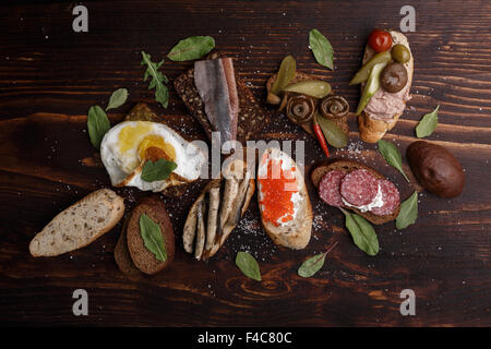 Verschiedene belegte Brötchen aus Vollkorn Baguette und Schwarzbrot mit verschiedenen Belägen über dunklen hölzernen Hintergrund. Stockfoto