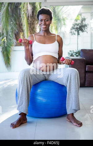 Porträt von lächelnden schwangere Frau mit Hanteln sitzen auf Gymnastikball Stockfoto