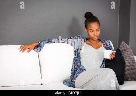 Teenager-Mädchen sitzen auf einem Sofa mit einer Tasse Kaffee oder Tee in der Hand. Stockfoto