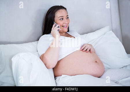 Schwangere Frau auf dem Bett liegend telefonieren Stockfoto