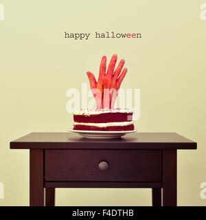 der Text happy Halloween und ein roter Samt-Kuchen mit einer blutigen Hand auf einem Tisch gekrönt Stockfoto