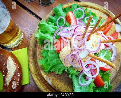 Obazda, Bayerische Creme Käsespezialität mit Zwiebel Ringe Tomaten, Salat, salzige Sticks, Brezel und Bier serviert Stockfoto