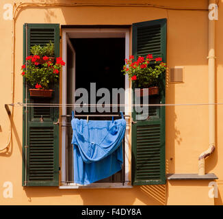 Italienischen Farben: Fenster mit offenen Fensterläden, rote geranie Vasen und blaue Wäsche hängen in der Sonne Stockfoto