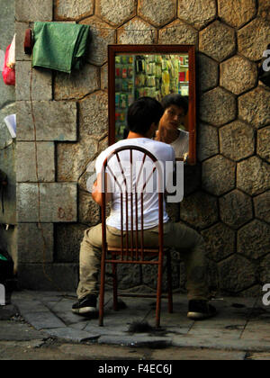 Junger vietnamesischer Mann mit einer Rasur mit einem Straßenbarbier Spiegel in Hanoi Stockfoto