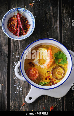 Weiße Keramik Pfanne mit würzigen Thai Tom Yam Suppe mit Kokosmilch, Chili-Pfeffer und Meeresfrüchten auf Keramik Schneidbrett über alte woo Stockfoto