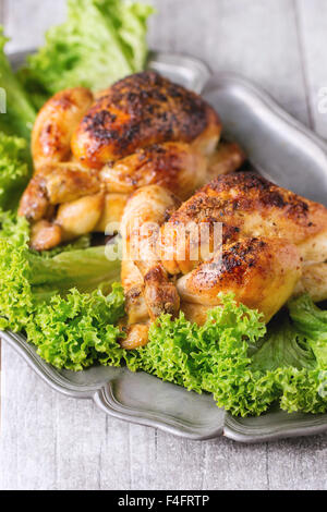 Nahaufnahme von Vintage Metall Schale mit zwei ganze gegrillte Hähnchen und grünem Salat über weißen Holztisch. Stockfoto