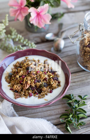 Ein Frühstück Einstellung mit einer Schüssel würzige Kürbis, Ahorn und Tahini-Müsli mit frisch gepflückt Blumen auf einem Bauernhof Stil Tisch. Stockfoto