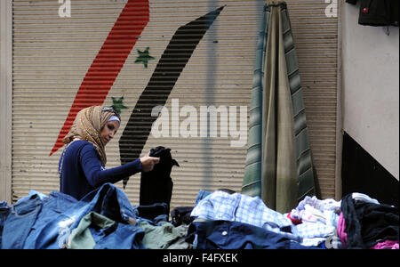 (151018)--Damaskus, 18. Oktober 2015 (Xinhua)--A Frau holt Kleidung an einem Stand in einem second-hand-Kleidung-Markt in Damaskus, Syrien, 17. Oktober 2015. Viele syrische Familien leiden unter hohen Arbeitslosenquote und ständig Inflation nach Jahren des Bürgerkriegs. Um das Budget abzuschneiden, entscheiden sich viele Damaskus Menschen abholen gebrauchte Mäntel und Schuhe für den kommenden Winter. (Xinhua/Zhang Naijie) Stockfoto