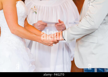 Braut und Bräutigam, Hände halten, während das Ja-wort am Tag ihrer Hochzeit in einer Scheune. Stockfoto