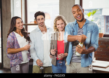 Mann öffnet Sektflasche mit Kollegen Stockfoto