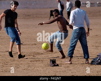 Multi-ethnischen Gruppe junger Männer, die Fußball spielen auf dem Strand, Weston-super-Mare, Somerset, Großbritannien Stockfoto