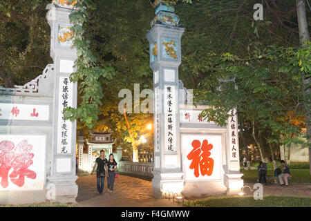 zwei Touristen verlassen die rote Huc Brücke und Eingang zum Tempel am Hoan-Kiem-See im Zentrum von Hanoi, die Hauptstadt, Vietnam Stockfoto