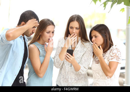 Vier besorgt Multi ethnischen Freunde beobachten ein Smartphone in der Straße Stockfoto