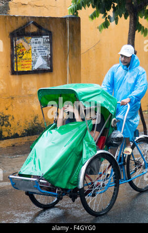 Cyclo-Fahrer gibt Touristen eine Fahrt im Oktober Regen Regen in Hoi an, eine antike Stadt in Vietnam an der zentralen Küste, Asien Stockfoto