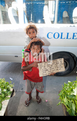 Ein Aeta Stammesangehörige Vater trägt sein Kind auf seinen Schultern halten ein Weihnachten Gruß in Tagalog - Filipino geschrieben. Stockfoto