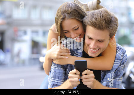 Paare oder Freunde lustig Lachen und Spaß mit einem Smartphone in einer großen Stadt Straße Stockfoto