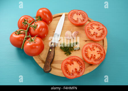 Geschnittene Tomaten zum Braten mit Wellenschliff, Knoblauch und Thymian auf Holzbrett Stockfoto