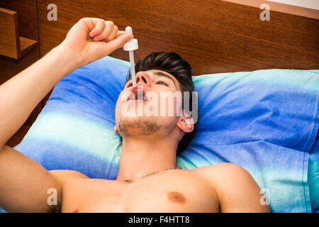 Krank oder unwohl junger Mann mit Pipette Pipette in den Mund für Medizin, medikamentöse Behandlung, beim liegen im Bett Stockfoto