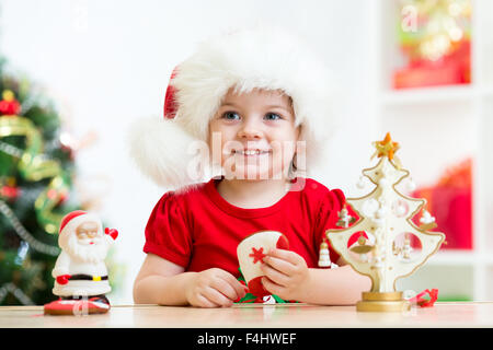 Kleine Mädchen tragen eine festliche rote Weihnachtsmütze mit Weihnachtsgebäck Stockfoto