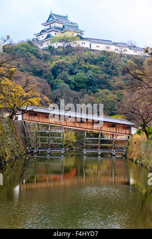 Japan, Wakayama Castle. Rekonstruierte Ohashiroka Brücke, ein seltenes Beispiel für eine überdachte geschlossene Brücke über den Burggraben, die Hügel im Hintergrund halten. Stockfoto