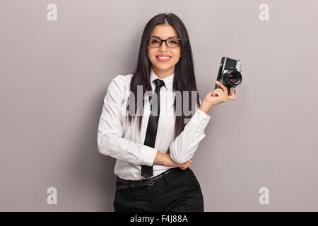 Fotografin mit schwarzen Brille hält eine Kamera und eine graue Wand gelehnt Stockfoto