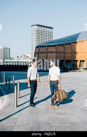 Zwei junge hübsche schwarze und blonde Haare modernen Geschäftsmann posiert in der Stadt, auf der Suche in die Augen, Lächeln - mit Spaß, Break, erfolgreiche, Business-Konzept Stockfoto