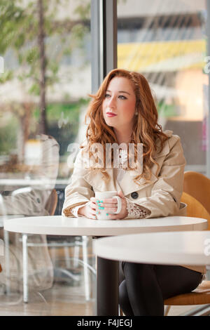 Mädchen sitzen in einem Café eine Tasse Kaffee halten, während Sie den Blick aus dem Fenster Stockfoto