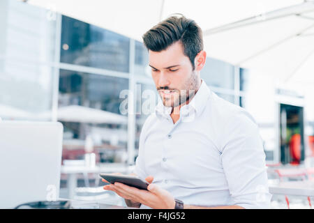 Porträt der moderne Geschäftsmann junge hübsche schwarze Haare, mit einem Tablet, auf der Suche nach unten und tippen auf den Bildschirm - Arbeit, Wirtschaft, Technologie-Konzept Stockfoto