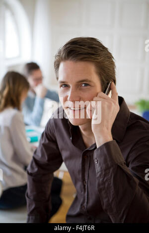 Porträt des jungen Geschäftsmann mit Mobiltelefon mit Kollegen im Hintergrund Stockfoto