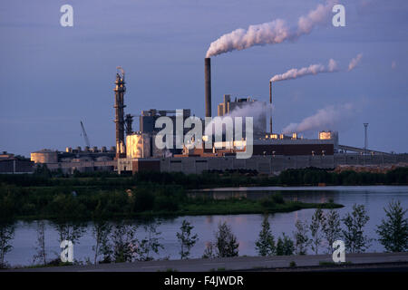 Fabrikschlot emittierende Rauch neben Fluss Stockfoto