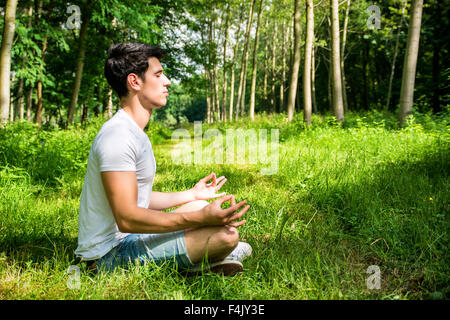 Profil von schönen jungen Mann während der Meditation oder tun ein Outdoor-Yoga Übung sitzen Cross Legged auf grasbewachsenen Boden allein in Stockfoto