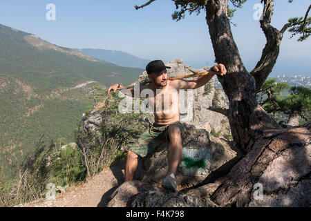 Junger Mann mit Rucksack auf Felsen sitzend und auf einen Blick Stockfoto