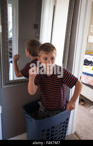 Kleiner Junge spielt und steht in seiner Heimat Flur in einen Wäschekorb Stockfoto