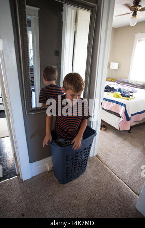 Kleiner Junge spielt und steht in seiner Heimat Flur in einen Wäschekorb Stockfoto