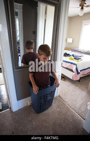 Kleiner Junge spielt und steht in seiner Heimat Flur in einen Wäschekorb Stockfoto