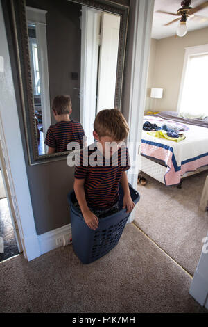 Kleiner Junge spielt und steht in seiner Heimat Flur in einen Wäschekorb Stockfoto