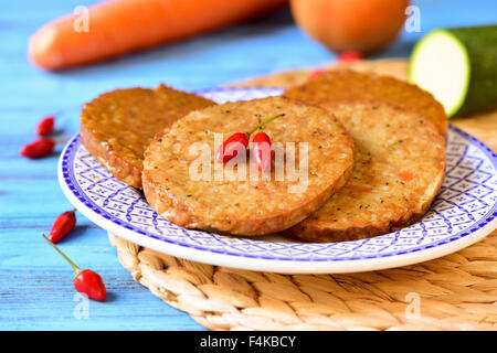 Nahaufnahme von einigen roh Veggie-Burger in einer Platte auf einem blauen Holztisch mit Gemüse im Hintergrund Stockfoto