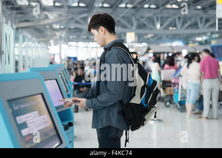 Junge asiatische Mann mit Self Check-in Automaten am Flughafen Stockfoto