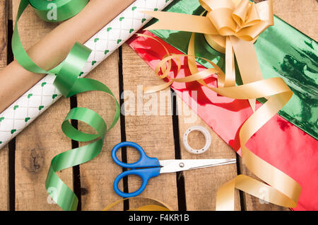 Geschenkpapier-Konzept mit verschiedenen Papierfarben, Schere, Klebeband und andere Decoratives liegen auf Holzuntergrund Stockfoto