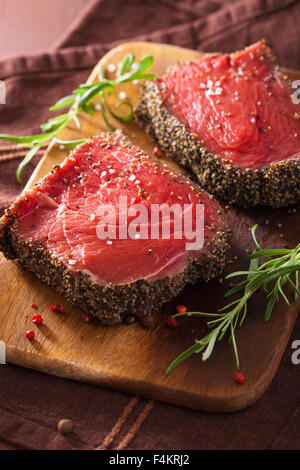 rohes Rindersteak mit Gewürzen und Rosmarin auf hölzernen Hintergrund Stockfoto