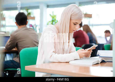 Porträt einer schönen Studentin am Tisch sitzen und mit Smartphone in der Universität Stockfoto