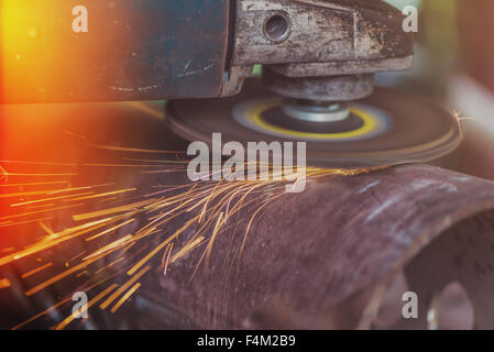 Arbeiter Schleifen Stahlrohr, Mann mit Schleifer auf Stück Metall in Werkstatt, Schleifen Funken fliegen herum, Retro getönten Arbeiten Stockfoto