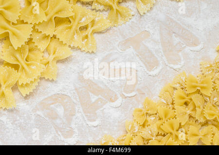 Inschrift auf dem Mehl Wort Pasta auf dem Brett mit Farfalle-Nudeln Stockfoto