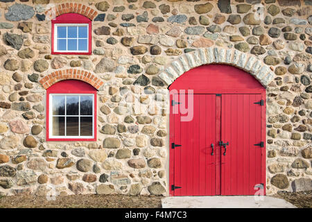 Hellrot gewölbte Tür und zwei verglaste Fenster legen Sie in einem alten Steinmauer.  Viel Textur, Farbe und Handwerkskunst. Stockfoto