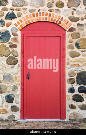 Leuchtend rot gewölbte Tür-Set in einem alten Steinmauer.  Viel Textur und Farbe. Stockfoto