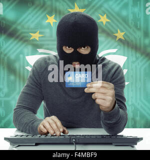 Dunkel-enthäutete Hacker mit Kreditkarte in der Hand und Flagge auf Hintergrund - Macau Stockfoto