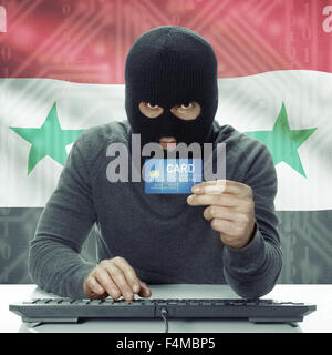 Dunkel-enthäutete Hacker mit Kreditkarte in der Hand und Flagge auf Hintergrund - Syrien Stockfoto