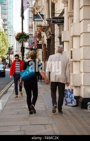 Älteres Paar in der Londoner Jermyn Street entlang, Hand in Hand und Einkaufstaschen in ähnlichen Farbtönen des Blaus. Stockfoto