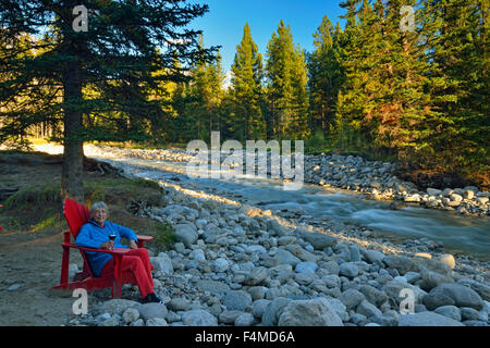 Frau mit Glas Wein entspannen entlang der Ufer des Baker Creek im Baker Creek Resort, Banff Nationalpark, Alberta, Kanada Stockfoto